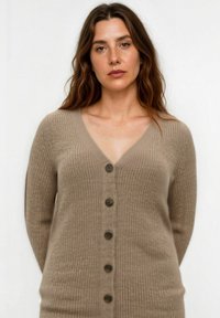 Beige gestrickte Strickjacke mit tiefem V-Ausschnitt, langen Ärmeln und sechs dunklen Knöpfen auf der Vorderseite sowie einem durchgängig gerippten Textur.