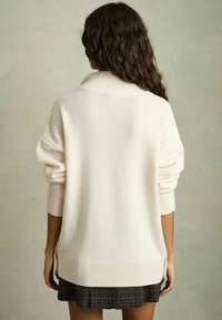 Pull crème surdimensionné en tricot doux avec un col et des poignets côtelés, présentant une ligne d'ourlet qui s'étend sur les côtés.