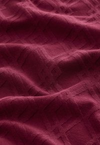 Burgundy textured fabric featuring a raised geometric pattern with diamonds and squares. Smooth surface with a soft, woven appearance.