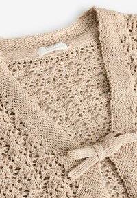 Cardigan lavorato a maglia beige con una trama aperta, adornato con paillettes argentate e chiusura annodata. Texture morbida e vestibilità rilassata.