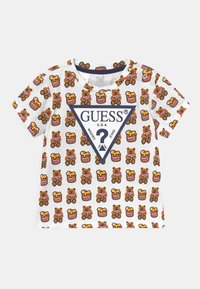 Witte t-shirt met korte mouwen, gekenmerkt door een patroon van een teddybeer en pot honing, met een blauw, driehoekig ‘GUESS’ logo aan de voorkant. Zachte katoentextuur.