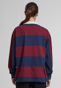 Dlhý rukáv polo tričko s horizontálnymi pásmi v bordovej a námorníckej modrej farbe. Vyrobené z jemnej bavlny s klasickým golierom a voľným strihom.