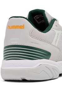 Weißer und grüner Sportschuh mit Obermaterial aus Netzgewebe, gepolstertem Schaftrand und gestreiftem Fersen-Design mit "hummel"-Branding in Orange. Strukturiertes Profil.