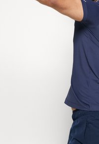 Námořnické sportovní tričko s krátkými rukávy, vyrobené z hladkého, lehkého materiálu. Má zaoblený výstřih a přiléhavý střih.