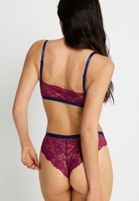 Bralette de encaje y braguitas a juego en un profundo burdeos con acentos de satén azul marino; patrón floral intrincado, textura semitransparente, tirantes ajustables.
