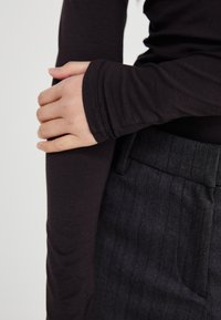 Tricou negru cu mâneci lungi și manșete ajustate, asortat cu pantaloni cu dungi subțiri texturate de culoare gri închis. Stil casual, linii curate și material moale.