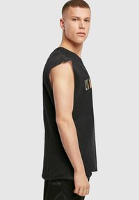 Melnas bezpiedurkņu T-krekls, kas izgatavots no kokvilnas, ar apaļu kakla izgriezumu un drukātu dizainu priekšpusē, ar mīkstu tekstūru un brīvu piegriezumu.