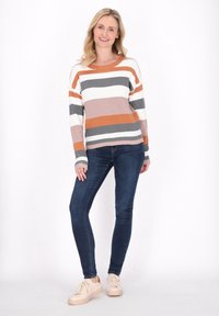Maglione a righe in toni caldi con texture a costine, abbinato a jeans scuri e sneaker di colore chiaro. Design semplice e di vestibilità rilassata.