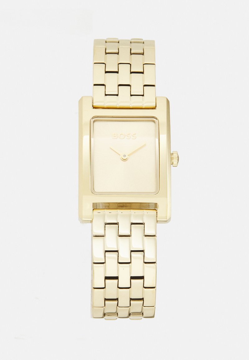Relógio retangular em tom de ouro com uma bracelete de metal polido, mostrador minimalista e uma sutil marcação no mostrador. Detalhe da coroa arredondada.