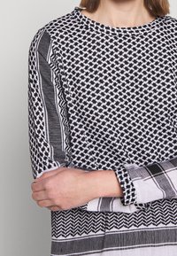 Blusa de estampado en blanco y negro que presenta un escote redondo, mangas largas con rayas en contraste y una variedad de diseños geométricos.