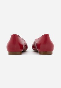 Ballerines en cuir rouge avec une texture lisse, un talon bas et arrondi, et un design simple, vues de l'arrière.