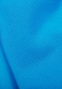 Jasnoniebieska dzianina o gładkiej fakturze i jednolitym wzorze małych, równomiernych ściegów. Brak widocznych wzorów lub elementów metalowych.