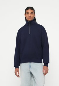 Marine blauw rits sweatshirt met een hoge kraag, een losse pasvorm, ribgebreide manchetten en een zoom, gecombineerd met lichtblauwe jeans. Zachte stof met minimale details.