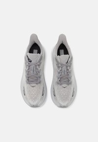 Scarpe da ginnastica grigio chiaro con tomaia testurizzata, dettagli in rete e lacci piatti. Presentano una suola imbottita e sottili accenti neri.