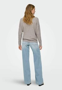 Pull léger gris, texturé, avec des épaules tombantes, associé à un jean bleu délavé à jambes larges. Le pull possède un ourlet et des poignets côtelés.