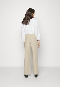 Calças largas bege com uma cintura elástica, combinadas com uma blusa branca. O tecido parece suave, com um ajuste descontraído e bolsos traseiros.