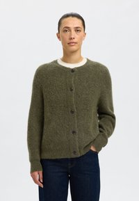 Olívazöld kötött kardigán, kerek nyakkivágással, elöl záródik fekete gombokkal, bordás mandzsettákkal. Puha, texturált anyag.