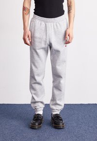 Gray sweatpants with an elastic waistband and cuffed ankles, made of a soft material. Worn with black shoes featuring fringe detailing.