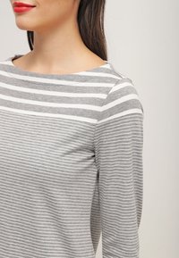 Haut à manches longues rayé gris et blanc avec un décolleté large, présentant une texture douce et une coupe décontractée.