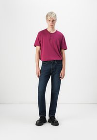Bordový polokrátky henley sveter s dvoma gombíkmi, v kombinácii s tmavomodrými džínsami a čiernymi masívnymi topánkami, na bielom pozadí.