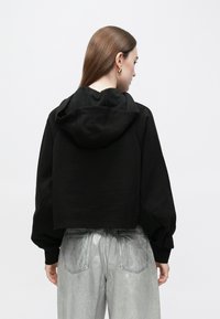 Camisola preta corta com capuz de cordão e mangas bufantes, combinada com jeans metálicos prateados com bolsos traseiros.