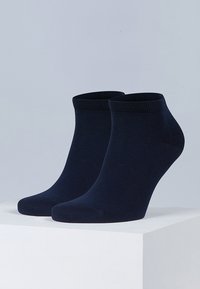 Calcetines de algodón azul marino hasta el tobillo exhibidos sobre una plataforma blanca, con un puño acanalado y una textura suave, sin patrones ni acentos visibles.