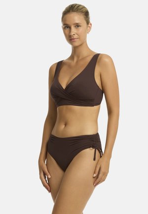 Model poseert in een bruine tweedelige bikini met een V-hals top en hoge taille broekjes, voor een effen witte achtergrond.