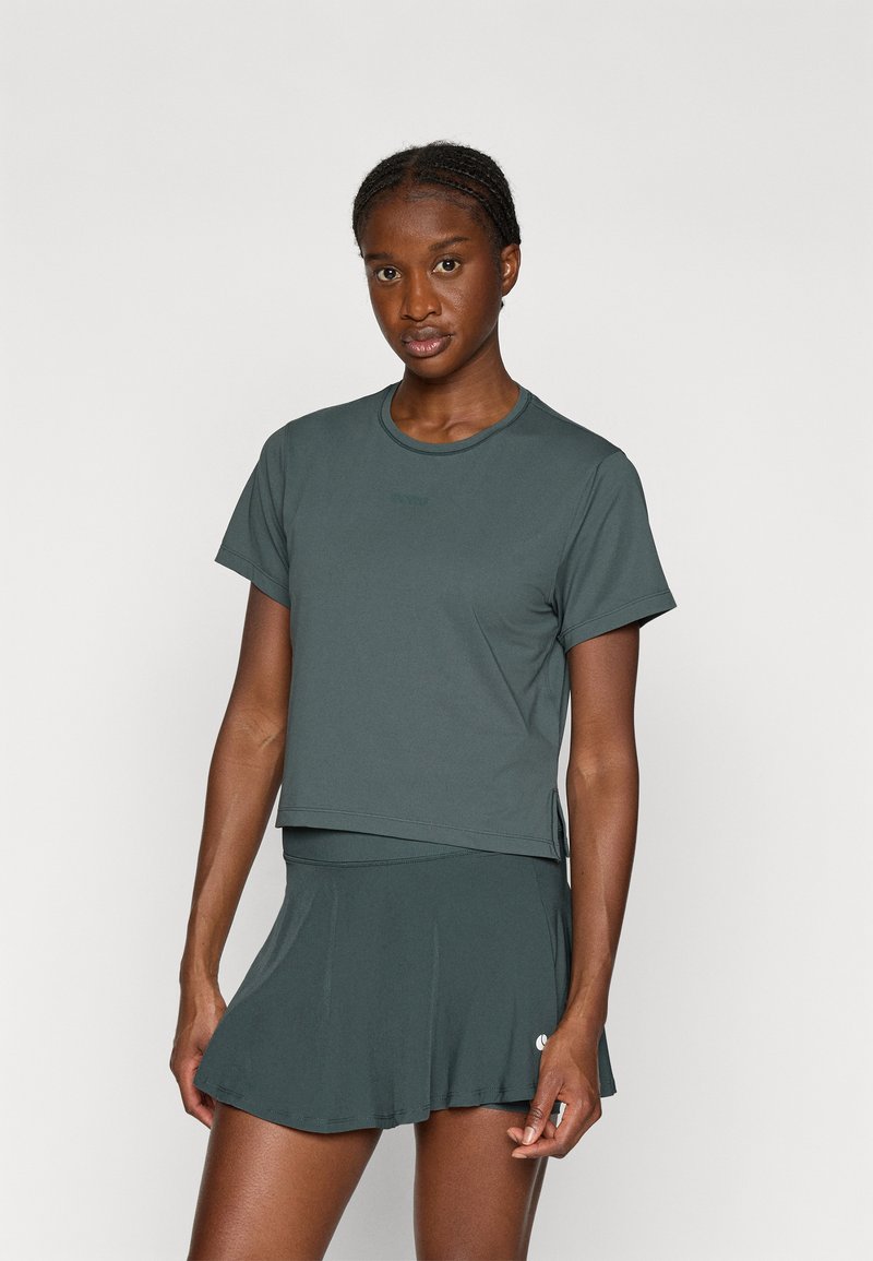 Tamnozelena sportska majica kratkih rukava s okruglim izrezom, u kombinaciji s odgovarajućom tamnozelenom suknjom u obliku A. Glatki, uski materijal.
