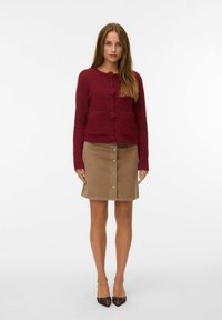 Burgundy texturerad kofta med runda knappar och två framfickor, tillsammans med en beige kordbyxa med framknäppning.