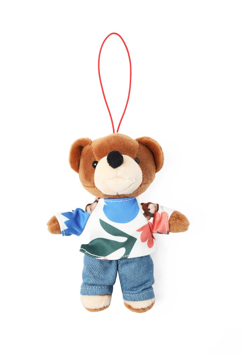 Plyšový medvídek jako přívěšek na klíče s hnědou kožešinovou tváří, oblečený v barevném květinovém tričku a modrých džínových kalhotách, má červenou zavěšovací smyčku.