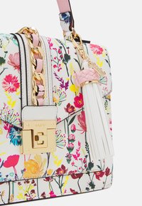 Sac à main imprimé floral en similicuir blanc. Il présente une quincaillerie dorée, une fermeture magnétique et un détail de pompon tressé rose et blanc.