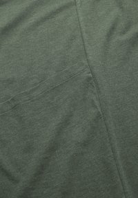 Dunkelgrüner Baumwollstoff mit glatter Textur, der eine sichtbare Tasche und subtile Nähdetails aufweist. Flach und gefaltet, ohne Muster.