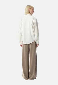 White button-up shirt with long sleeves, featuring a relaxed fit and a back yoke detail, paired with wide beige trousers.