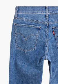 Blå jeans i denim med en klassisk design som har två bakfickor, synliga sömmar och en röd varumärkesflik på den högra fickan.