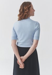 Light blue short-sleeve top with a fitted design and ribbed accents, paired with a black skirt. Hair is styled in loose curls.