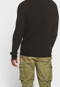 Pull noir en maille avec une finition texturée, doté de manches longues et de poignets côtelés, associé à un pantalon cargo vert olive avec poches latérales.