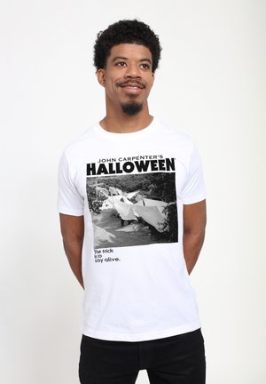 Bílý bavlněný tričko s černobílým grafickým potiskem z "Halloween" Johna Carpentera, s tučným textem a jednou řádkovou citací níže.
