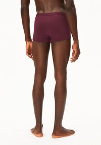 Burgunderfarbene, enganliegende Boxershorts mit einem weichen Bund, glatter Textur und einer Länge bis zur Mitte des Oberschenkels, von hinten an einem barfüßigen Modell gezeigt.