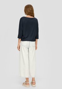 Marineblauwe, loszittende top met driekwart mouwen, gecombineerd met hoog-waist, wijde witte denim broek. Sandalen met een geknoopte uitvoering.