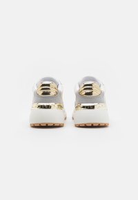 Sneakers with a white and gray upper, featuring a shiny gold heel accent and embossed brand name. Thick white sole with a rubber outsole.