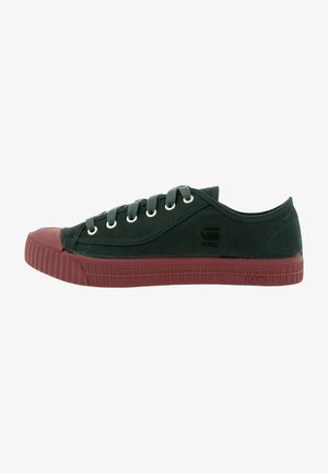 Zapatilla baja de lona verde oscuro con suela y puntera de goma color granate, ojales metálicos y "RAW" grabado en la suela.
