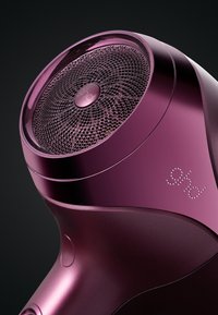 Haardroger met een glanzende, diep paarse behuizing, een ronde gaasrooster en een soepele ergonomische handgreep. Heeft het merk "ghd" in metallic detail.