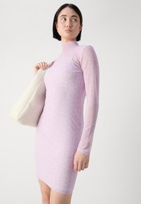 Long-sleeve, fitted dress in light purple with a textured pattern. Model holds a light-colored handbag, set against a neutral background.