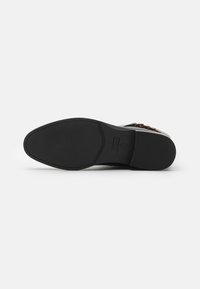 Suela de goma negra con agarre texturizado, con un diseño plano. La parte superior tiene un contorno elegante y detalles de hardware metálico.