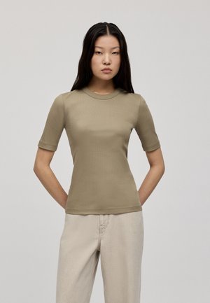Kortemouwen, aansluitend top in olijfgroene ribbelstof met een ronde hals. Het model draagt lichtbeige, comfortabele broek.