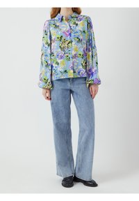 Kwiatowa koszula na niebieskim tle, z długim rękawem i kołnierzykiem, zestawiona z jasnoniebieskimi spodniami w kant i czarnymi butami.