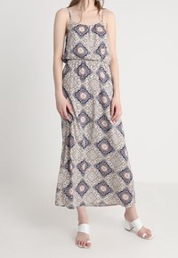 Robe maxi avec un motif géométrique complexe en crème, bleu marine et bourgogne. Comprend des bretelles fines, une taille élastique et une silhouette fluide.
