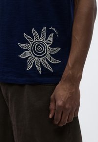 Μπλε ναυτικό T-shirt με λευκό κεντητό σχέδιο ήλιου στο κάτω αριστερό μέρος. Κοντά μανίκια, στρογγυλή λαιμόκοψη, ύφασμα από βαμβακερό μείγμα.