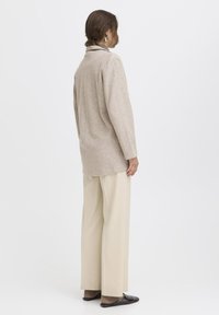 Beige gebreid longsleeve shirt met kraag, relaxed fit, gecombineerd met cream kleurige broek met wijde pijpen en donkere instap schoenen.