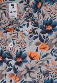 Shirt met een blauw, oranje en grijs bloemenpatroon, witte en oranje knopen, en het J&JOY merklabel "Ontworpen in België."
